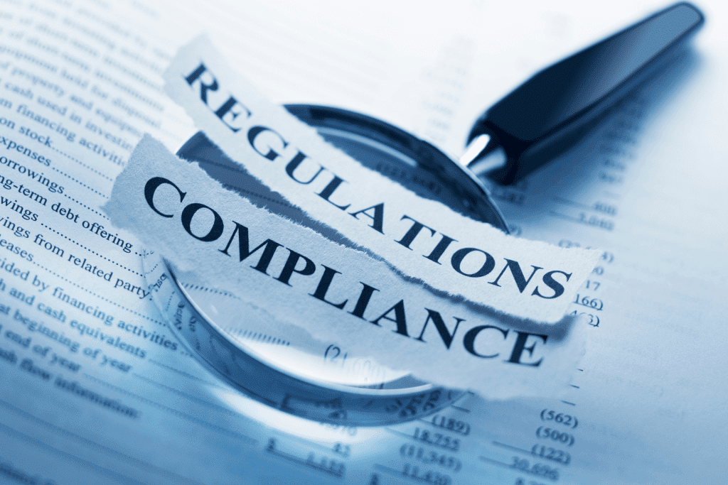 A magnifying glass on top of a document that has torn out pieces of paper on top of it that say "regulations" and "compliance".