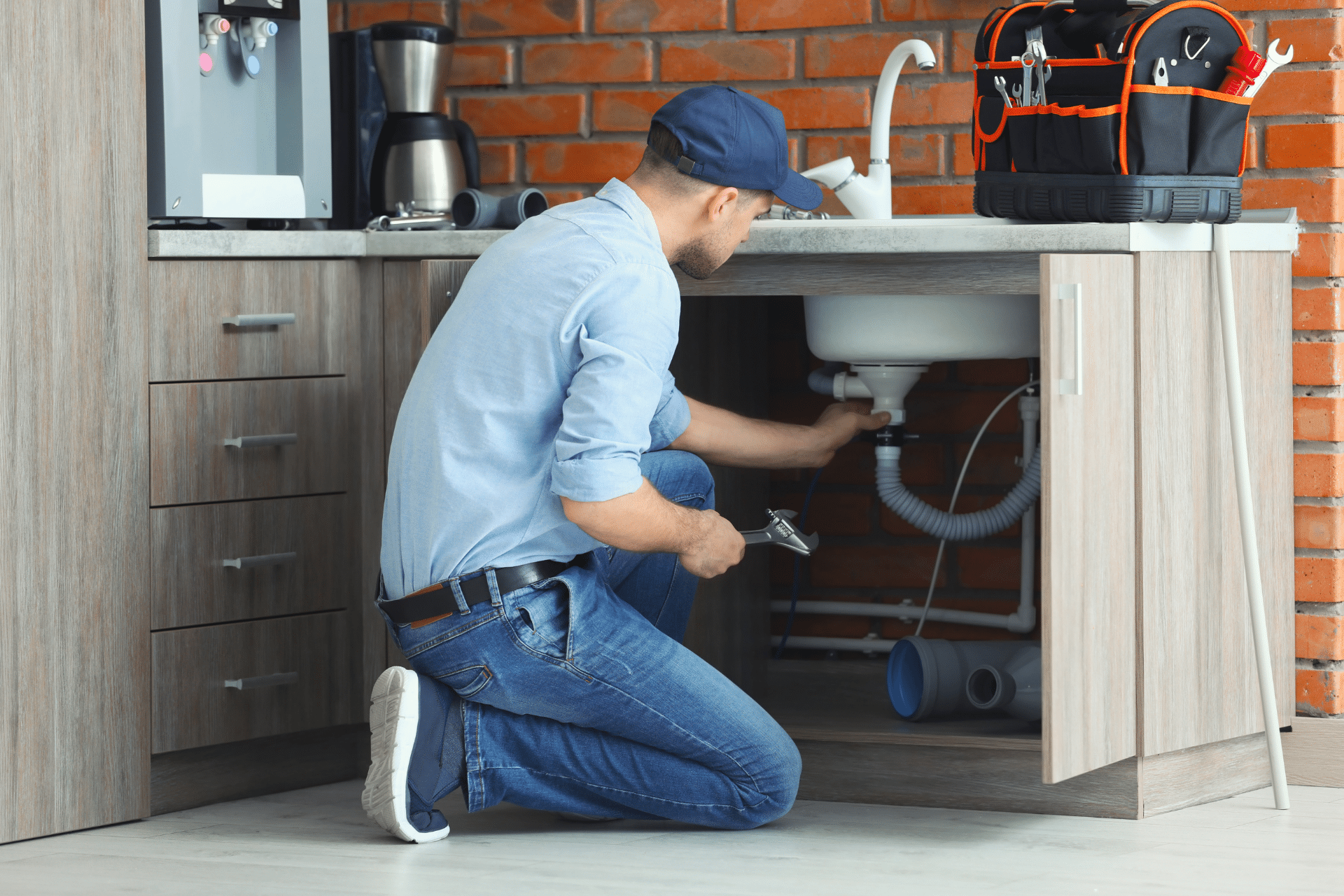 A man in a blue shirt performing plumbing repairs on a bathroom sink.