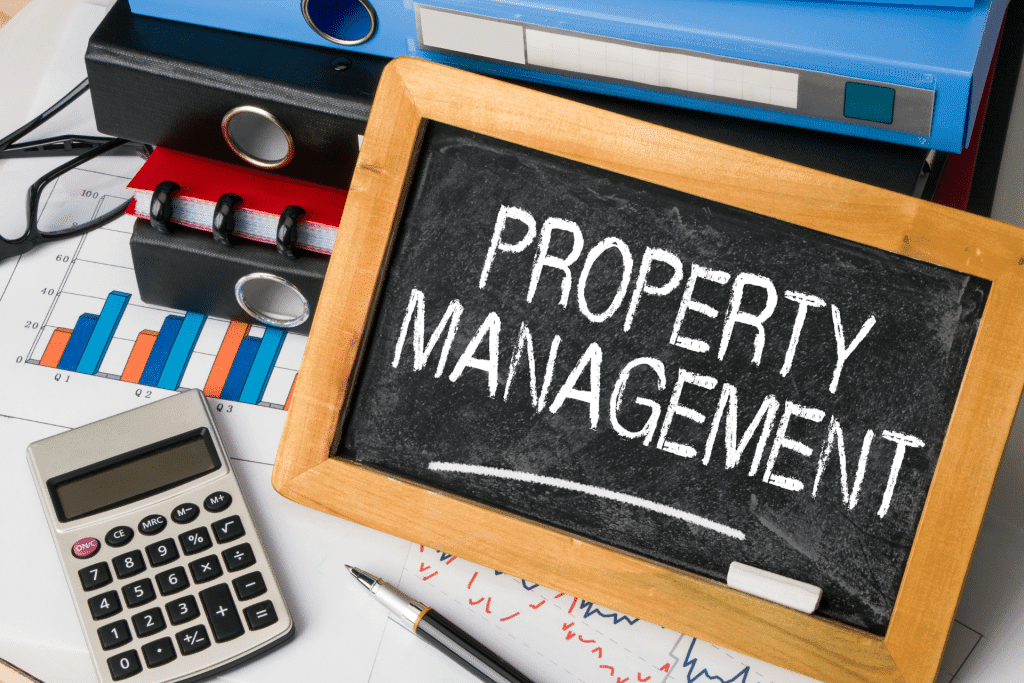 A chalkboard sign with the words property management on it. The sign is sitting on a desk with a calculator, pen, and other items.
