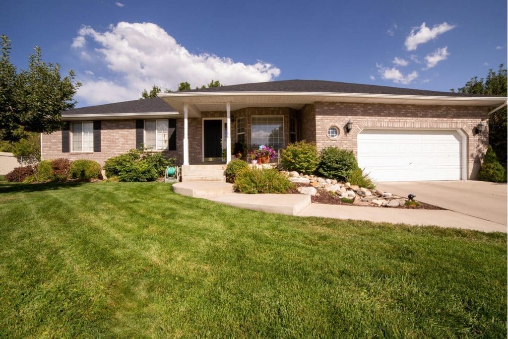 A well-maintained house with a gray roof, white garage door, four front glass windows, a brown door, and a green front yard, illustrates the importance of property maintenance tips for rental properties