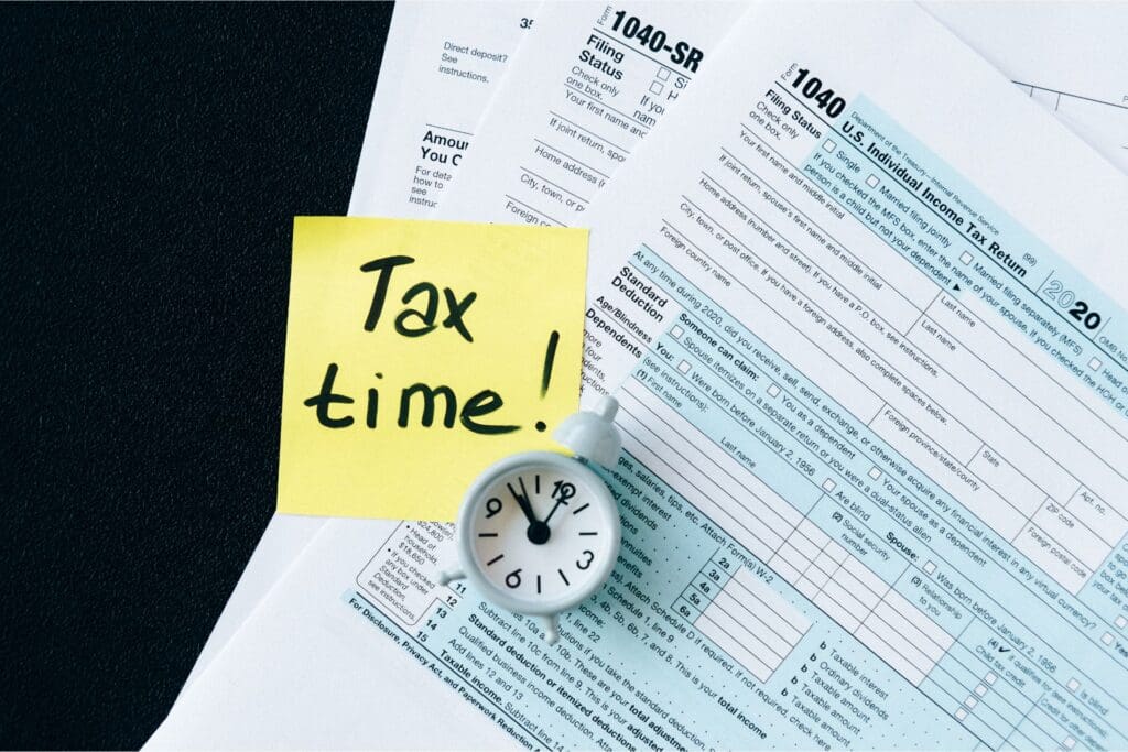 Close-up of 1040 tax forms with a 'Tax time!' sticky note and a clock, emphasizing rental property tax deductions and tax season urgency.