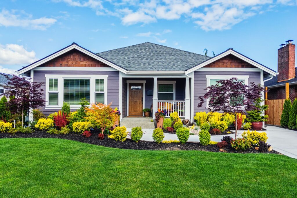 A house in Austin purple exterior, wood accents, and white trim, featuring a small porch, colorful landscaped shrubs and flowers, and a concrete driveway illustrating how to manage your first rental property in Austin.
