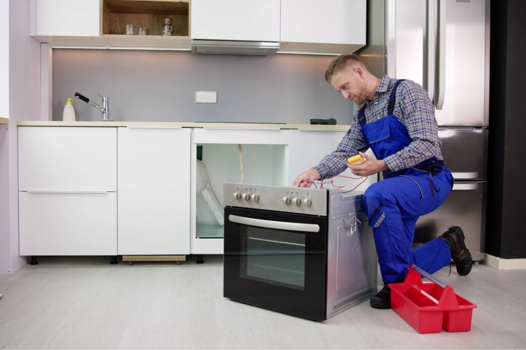 Appliance repair technician testing electric oven wiring in modern kitchen, illustrating landlord appliance responsibilities.