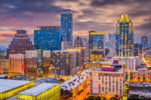 An urban skyline at dusk with illuminated skyscrapers and diverse architecture, representing the vibrant scene managed by a Property Manager in Austin TX.