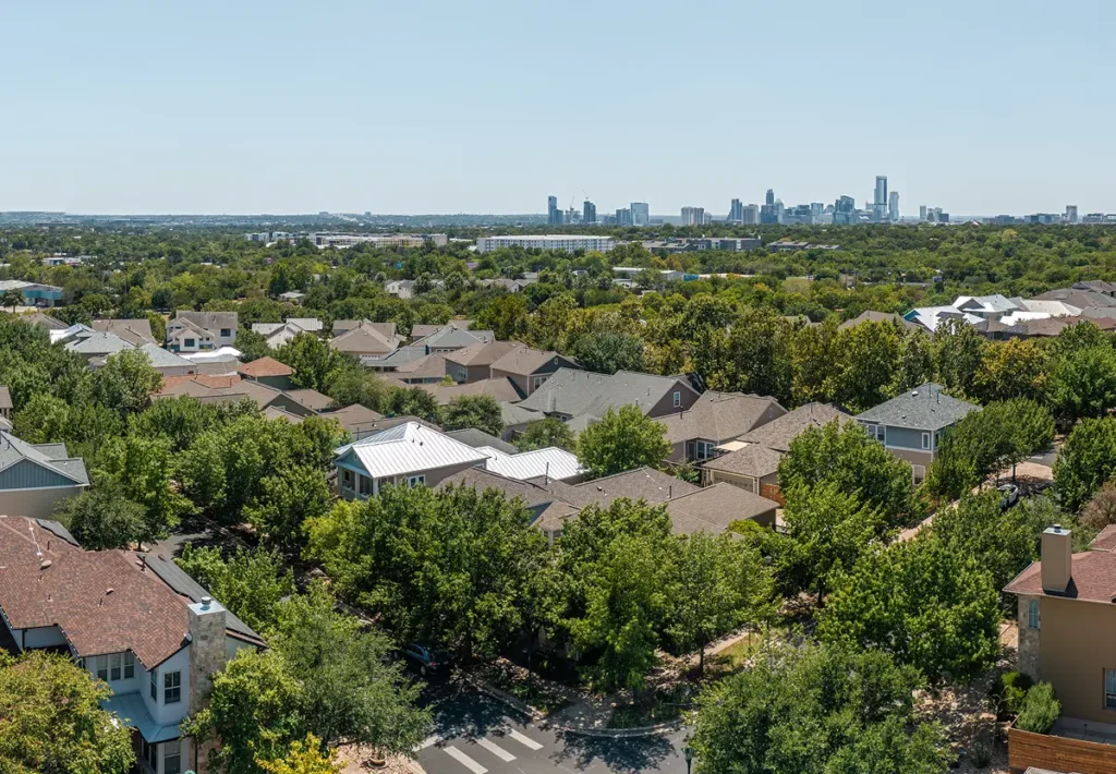 Aerial view of a residential neighborhood of single-family homes with the downtown Austin skyline on the horizon, illustrating affordable suburbs within commuting distance of the city