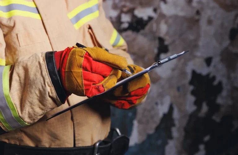 Fire investigator in protective gear documenting damage on a clipboard after a house fire